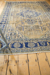 Navy blue border, worn ivory field texture, and natural fringe of the Oushak carpet.