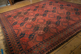 Angled view of vintage Ersari rug with cochineal red field, navy geometric medallions, and diamond border.