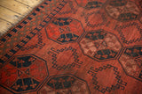 Vintage Ersari rug detail with cochineal red geometric medallions, navy border, and light tatter on selvage.