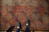 Feet on antique Ersari carpet, showing worn cochineal red and indigo geometric patterns.