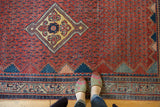 An overhead perspective of a vintage Serbend rug's textured red boteh field and detailed border.
