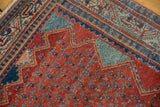 Corner view of a vintage Serbend rug showing its zigzag border, red field, and low pile.