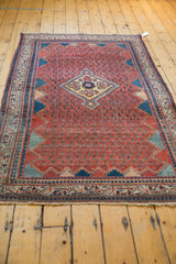 A vintage Persian Serbend rug viewed at an angle, showing its red boteh field and diamond medallion.
