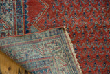Folded corner of a vintage Serbend rug revealing its hand-knotted back and boteh pattern.