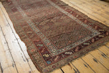 Corner detail of a hand-knotted antique Kurdish rug, showing tattered ends and border artistry.