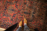 Dusty brick red field of vintage American Sarouk rug, allover navy floral pattern, showing wear.