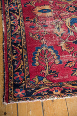 Detail of vintage Lilihan rug's cherry red field, navy border, germinating plants, and tattered fringe.