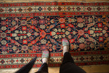 Feet on vintage Malayer runner, highlighting Henna plant lattice on navy field, with even wear.