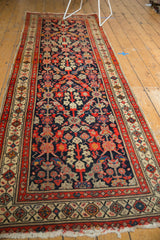 Detail of Malayer rug's colorful henna plant design, geometric border, and tattered fringe end.