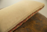 Antique rug fragment pillow side, showing light beige cotton and woven coral and sage geometric edge.