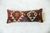 Geometric pattern detail on antique Kilim rug fragment lumbar pillow in rich red, navy, and cream.