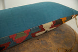 Teal fabric meets antique Kilim lumbar pillow fragment featuring geometric red, blue, beige patterns.