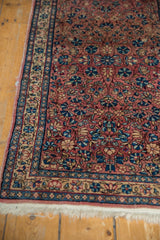 Persian Kerman rug corner showcasing dusty red floral field, intricate blue and ivory border, and fringe.