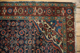 Vintage Hamadan rug corner with navy Herati motif, contrasting red borders, and worn fringe.