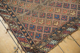 Antique Caucasian rug fragment corner, showing geometric patterns, aged tattered edges, and exposed foundation.