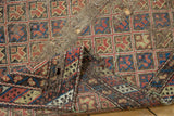 Tattered antique Caucasian rug fragment, showing exposed foundation and geometric red, blue, and gold pattern.