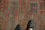 Feet on antique Caucasian rug, showing worn pile, geometric medallion, and crab motifs.