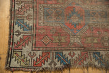 Antique Caucasian rug corner with brick red and blue geometric motifs, worn pile, tattered fringe.