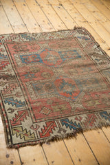 Antique Caucasian rug corner, displaying geometric patterns, visible wear, and tattered fringe.