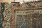 Distressed corner of an antique Caucasian rug, with serrated leaf border and geometric patterns.