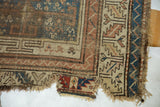 Tattered edge, wear, holes, and visible patch on antique Caucasian runner.