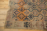 Antique Caucasian rug corner: threadbare tangerine and blue patterns, tattered fringe.