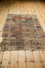 Threadbare antique Caucasian rug fragment featuring geometric multi-medallion design in tangerine, blue, and sand tones.