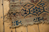 Antique Caucasian rug's threadbare corner, geometric blue, red motifs, and frayed edges.