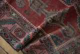 Detailed weave of a folded antique Karabagh rug showing its serrated leaf border and geometric motifs.