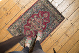 Antique Kerman mat shown to scale, highlighting its time-softened texture and fuchsia floral medallion.