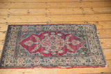 Antique Kerman mat with time-softened wear and visible tatter along its floral bordered edges.