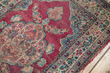 Detail of an antique Kerman rug showing its hand-knotted texture, abrashed fuchsia field, and scalloped floral border.