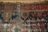 Tattered end of antique Malayer rug, revealing geometric borders and worn pile.