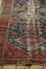 Close view of prominent wear on an antique Malayer rug, revealing foundation and faded red, blue motifs.