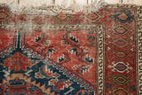 Corner of antique Malayer rug, showing worn fringe, aged texture, and red, blue, ivory motifs.