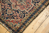 Corner of vintage Hamadan rug, showing navy floral field, intricate borders, and tattered side finish.
