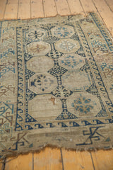 Antique Caucasian rug close-up: geometric border, ivory, blue, hard wear, tattered edge.