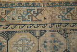 Worn antique Caucasian rug fragment with geometric patterns in beige, blue, and brown.