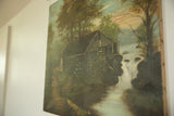 Angled view of vintage painting with a stone cottage, river, and visible canvas texture.