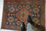 Overhead view of an antique Tehran rug, highlighting the worn texture of its red and indigo geometric pattern.