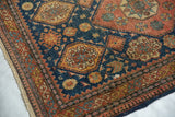 Angled view of the antique Tehran rug's corner, showing its tattered side and intricate border design.
