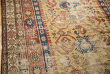 Angled view of antique Caucasian rug's saffron field, geometric motifs, terracotta borders, and wear.