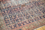 Worn end of an antique Malayer rug runner showing navy, blush patterns, exposed foundation, and fringe.