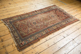 Antique Kurdish rug with geometric diamond medallions, hook and latch border, and visible edge wear.