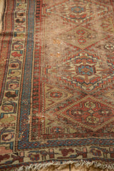 Time-softened geometric motifs and blue border on an antique Kurdish rug.