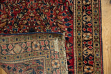 Vintage American Sarouk rug corner showing red floral pile, hand-knotted foundation, and tattered end.