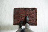 Antique Mohajeran Sarouk rug's plum and navy floral pattern, with boots on worn pile.