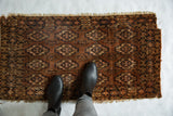 Detail of antique Turkmen rug's chestnut field with repeating navy blue floral guls and worn fringe.