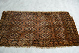 Repeating floral gul motifs in chestnut, navy, and ivory on an antique Turkmen rug with tattered fringe.