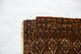 Antique Turkmen rug corner featuring tattered edge, fringe, and chestnut, navy, ivory guls.